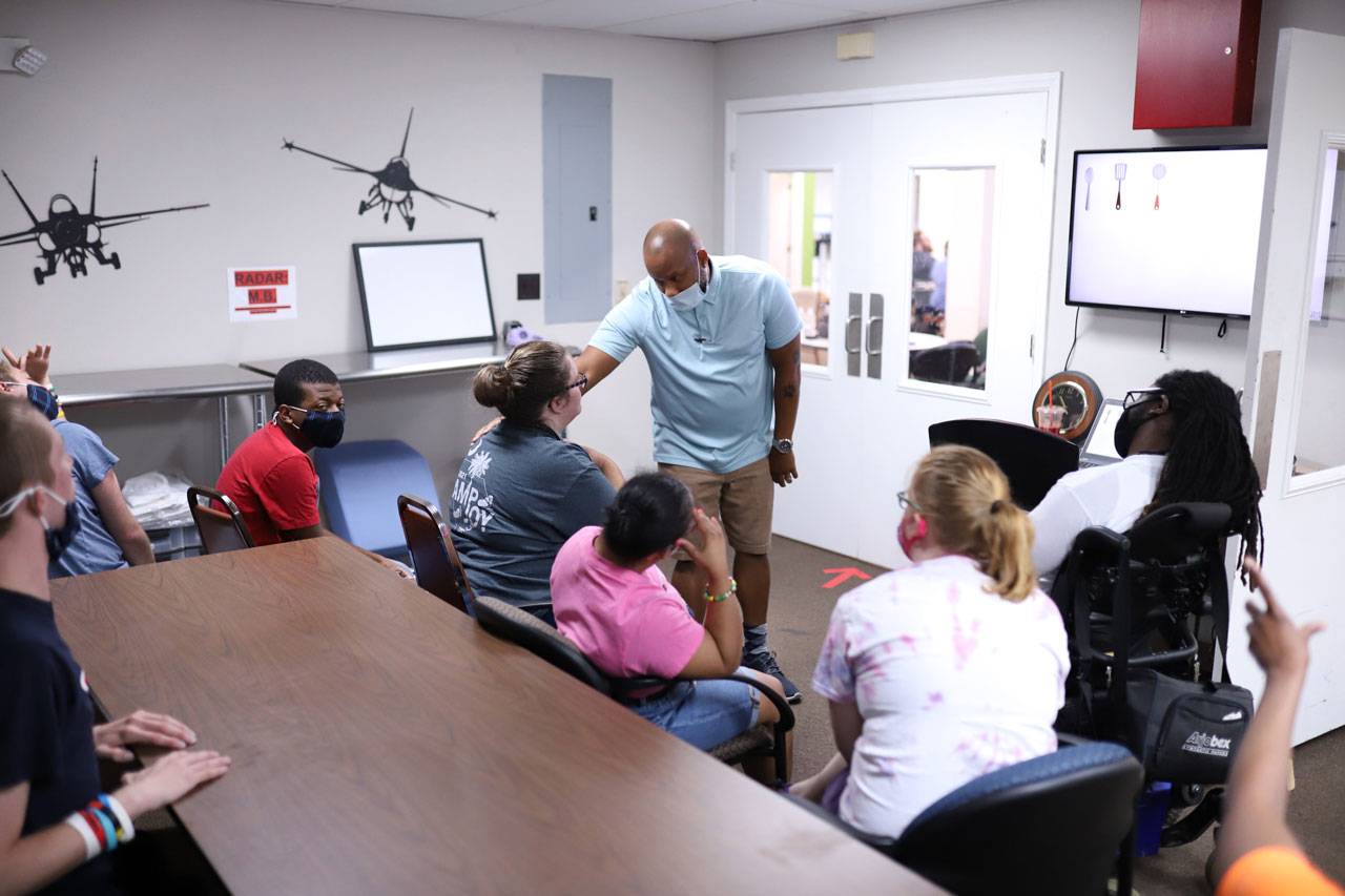 Adult Enrichment Center staff member in a light blue shirt addressing a seated group of program members