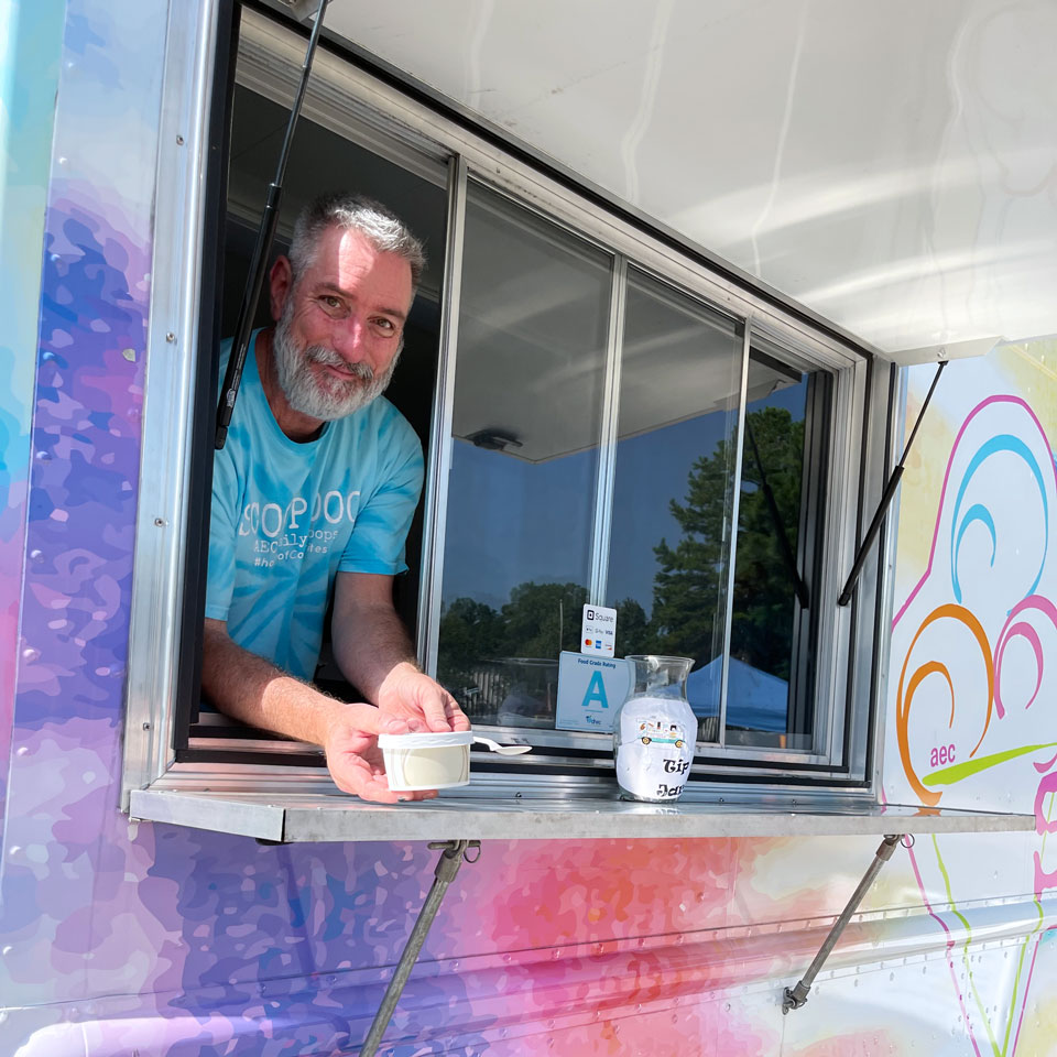Manager and Operator of Daily SCOOPS Mark Kriegshauser holding small cup of ice cream and smiling from SCOOPS truck window