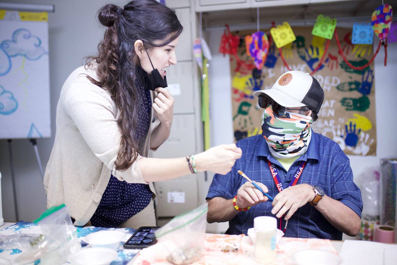 High5 day program for adults with disabilities staff member explaining an activity to a member in the colorful craft room