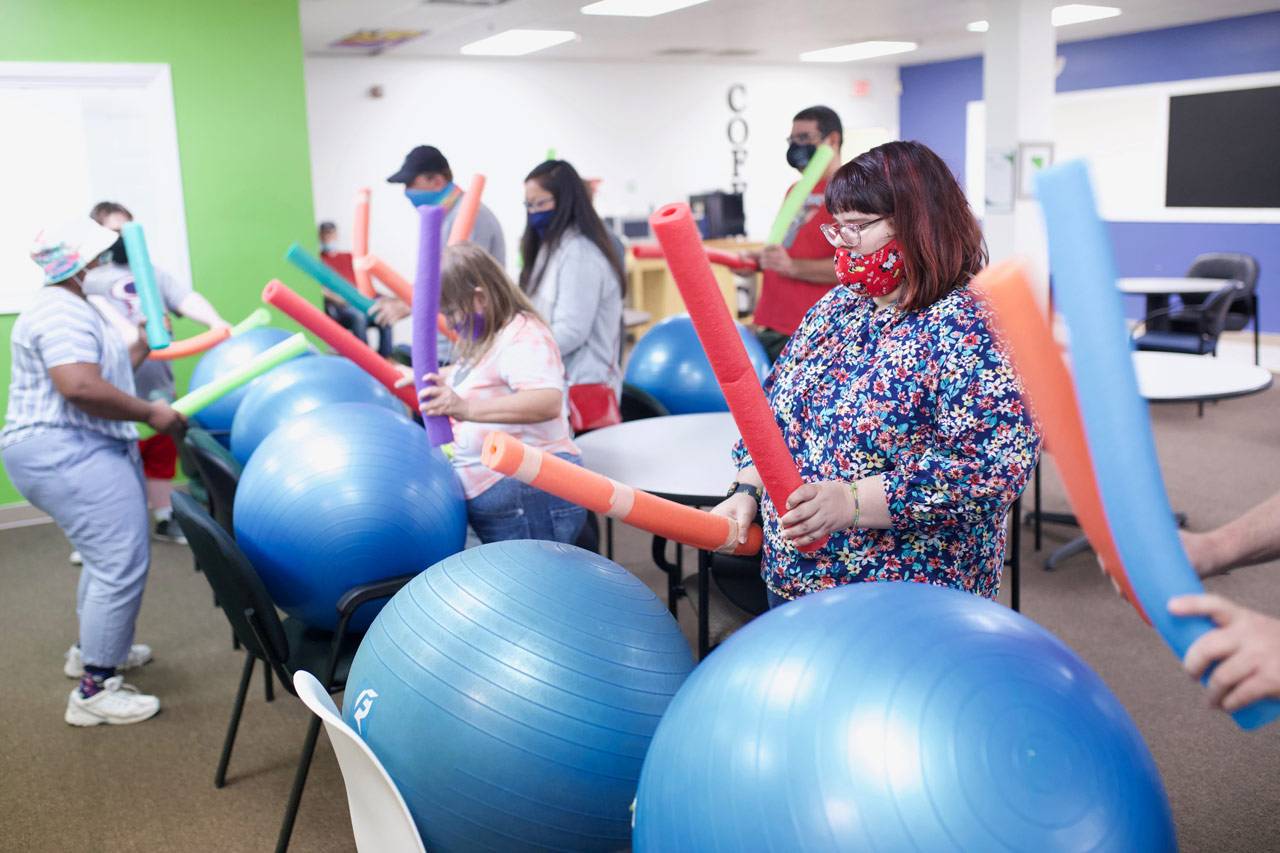 Members of the High5 day program for adults with disabilities tap brightly colored pool noodles against large blue exercise balls