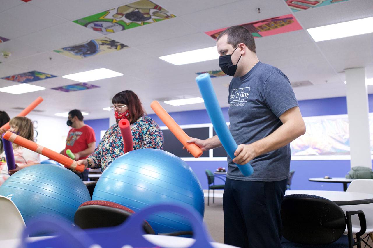 Male and female member of the High5 day program for adults with disabilities hold brightly colored pool noodles above large blue exercise balls
