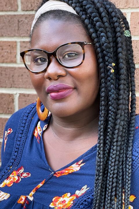 Head shot of Assistant Director of High5 Lydia Wylie with long braided hair, wooden hoop earrings, and blue floral blouse