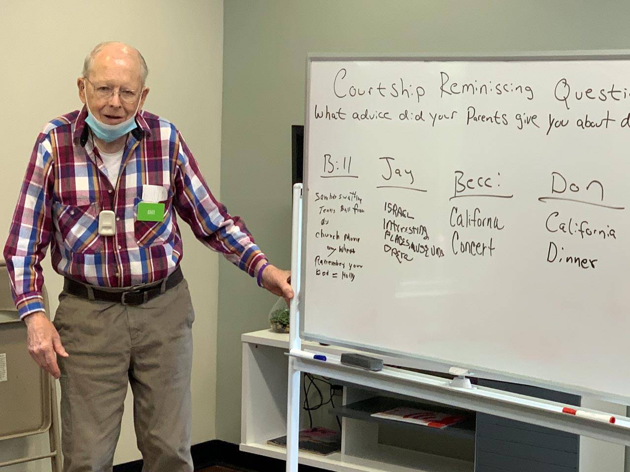Renew dementia daycare member Bill stands in front of white board during an activity with courtship reminiscing questions