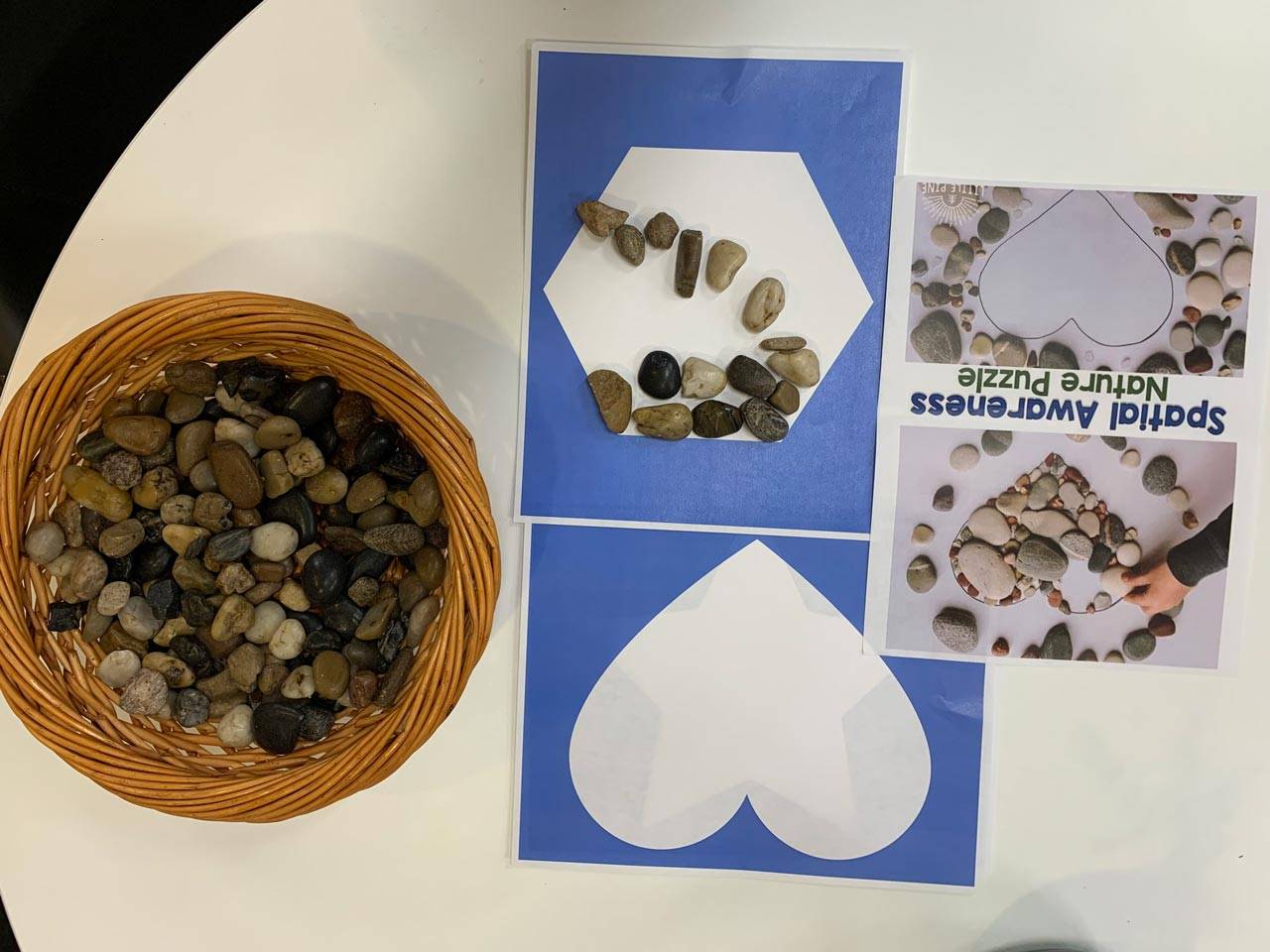 Renew dementia day care activity to complete a nature puzzle that includes white shapes on a blue sheet of paper to be filled with stones
