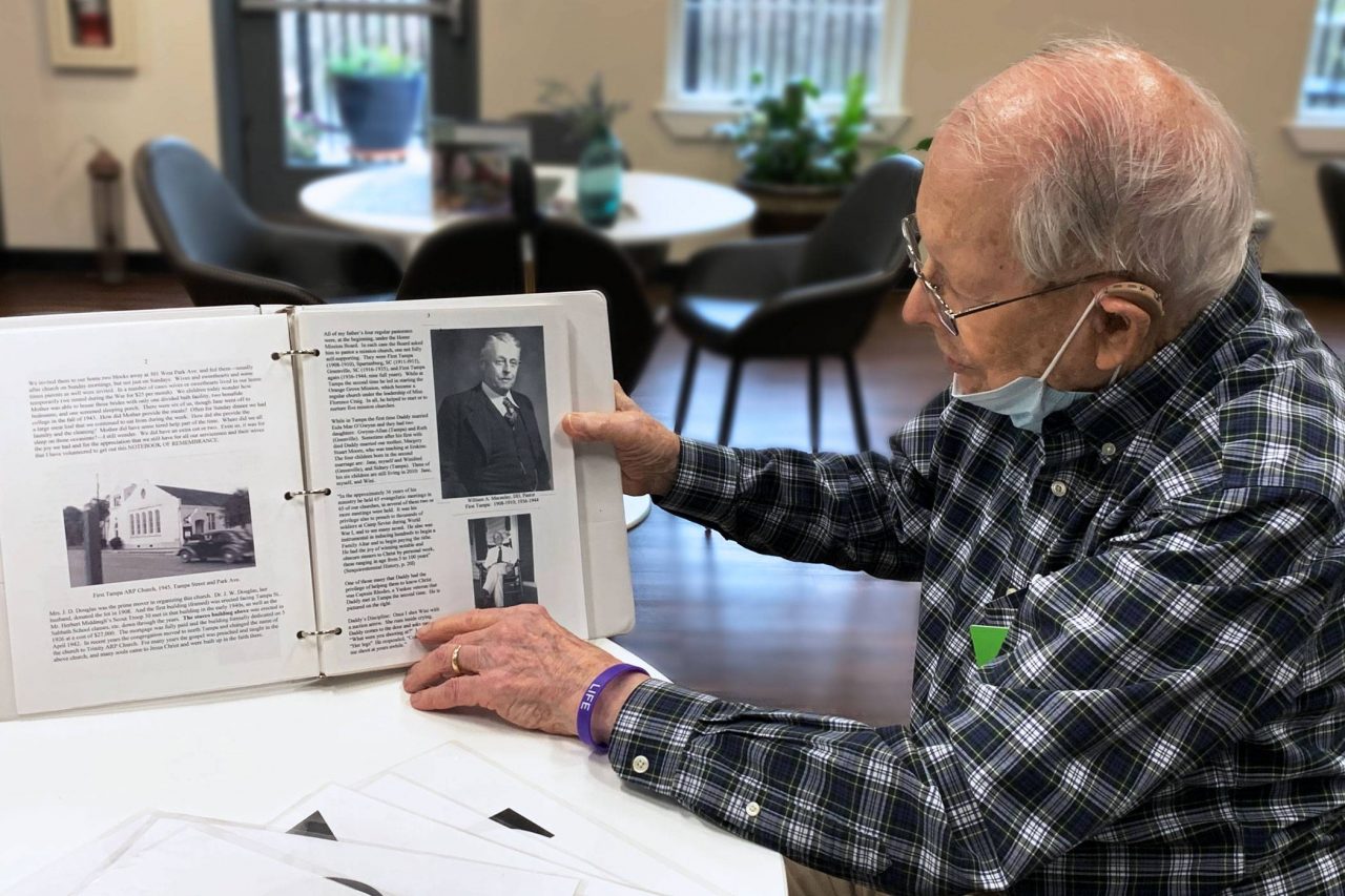 Elderly member of renew Montessori center for aging and memory holding binder with page opened to black and white photo from early 1900s