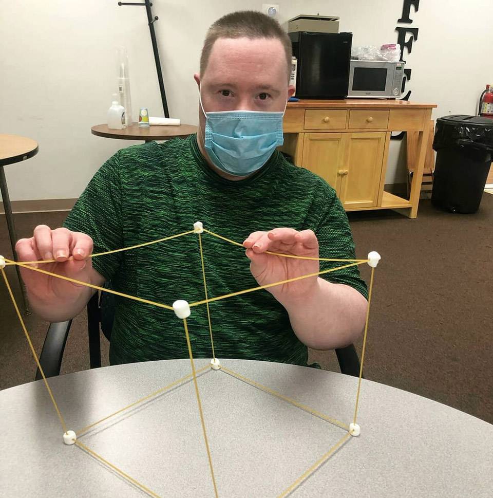 Male member of thrive adult daycare showing off 3-d cubic structure built from dry spaghetti noodles and marshmallows