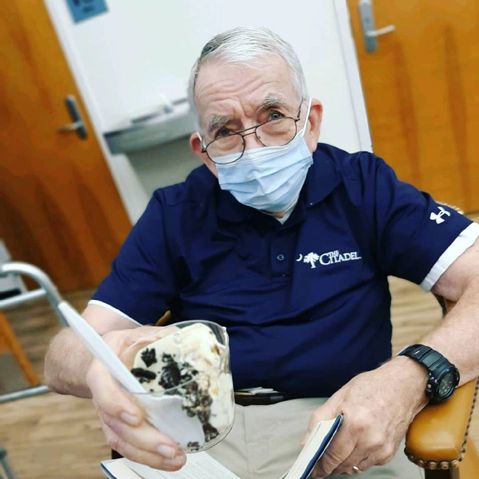 Elderly male member of thrive adult day health care wearing blue Under Armour polo embroidered with the Citadel logo holds up cup of cookies and cream ice cream