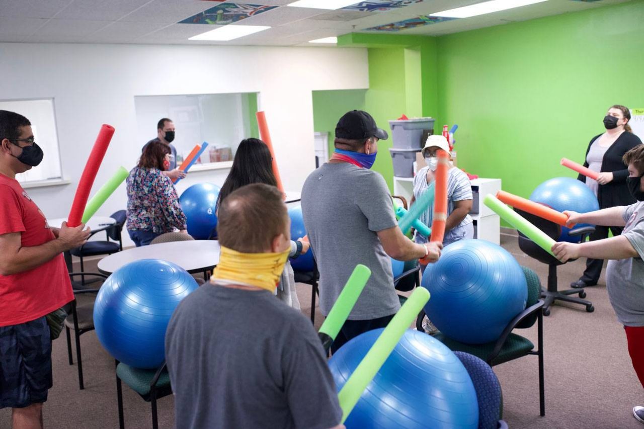 Members of the High5 day program for adults with disabilities hold brightly colored pool noodles above large blue exercise balls