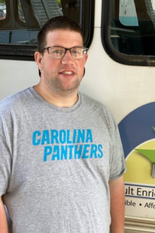 High5 Works member Cameron wearing Carolina Panthers gray T-shirt smiling